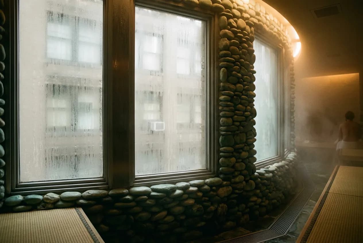 Close view of jade-toned sauna stones and condensation on glass inside a dim steam room