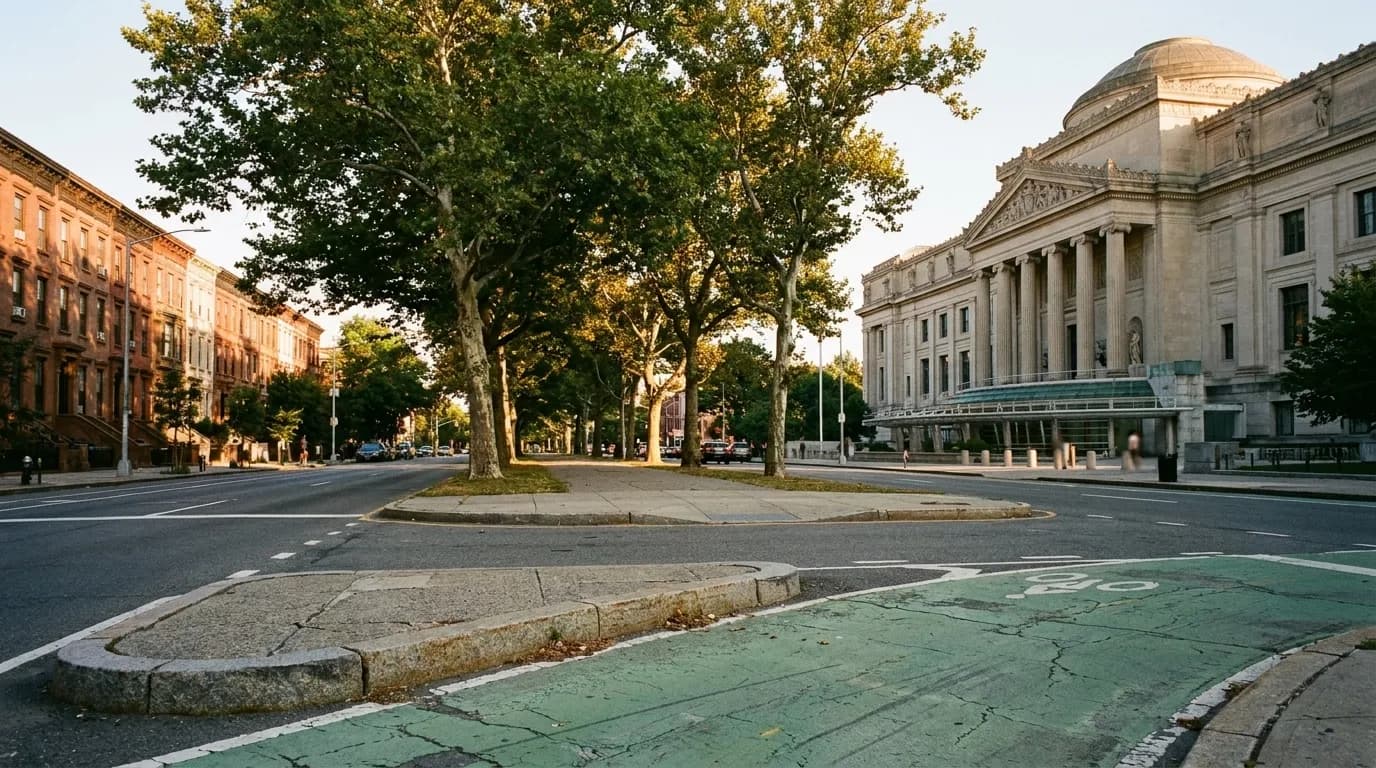 Eastern Parkway in Crown Heights looking toward the Brooklyn Museum on a late afternoon, with London plane trees and Beaux-Arts architecture in golden hour light.