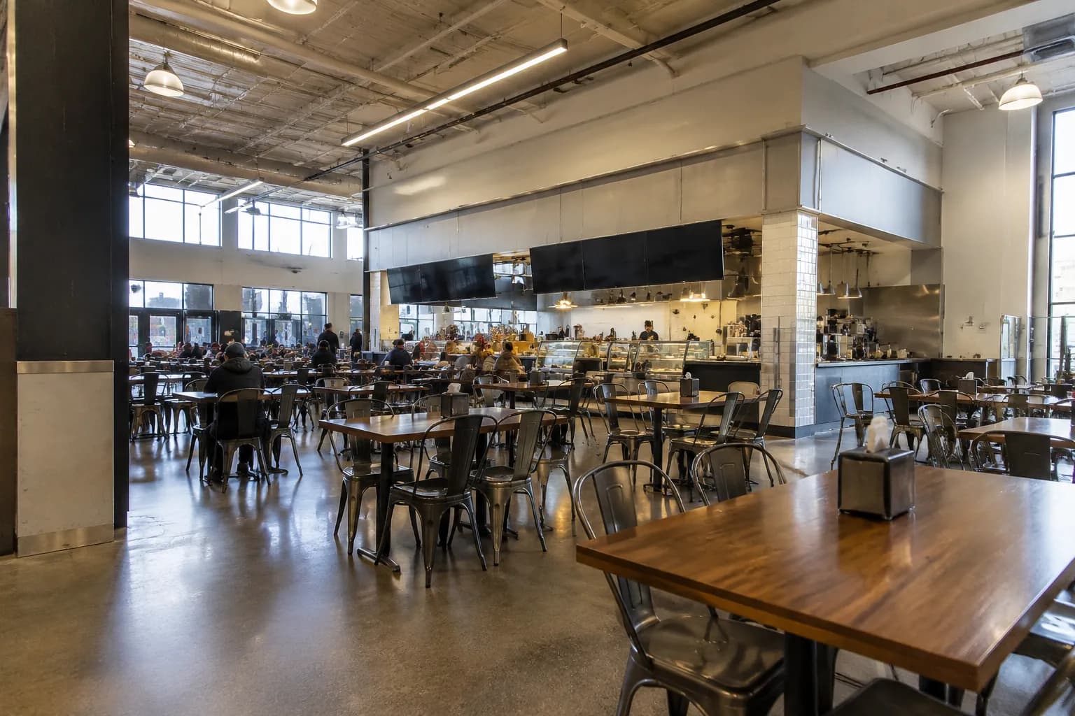 Communal seating area inside Essex Market with wooden tables and vendor stalls