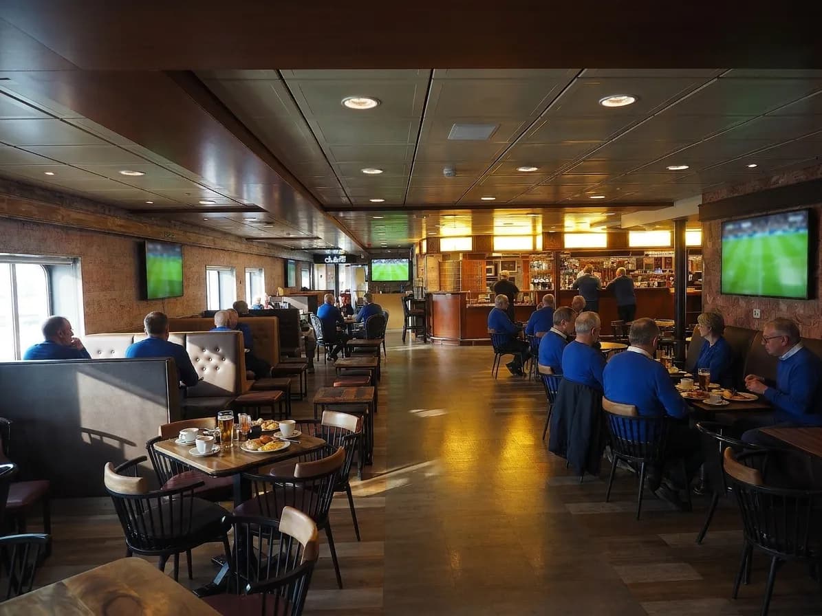 A pub at half past seven in the morning with the lights on and a match playing, a dozen people in blue at tables with coffee and breakfast plates