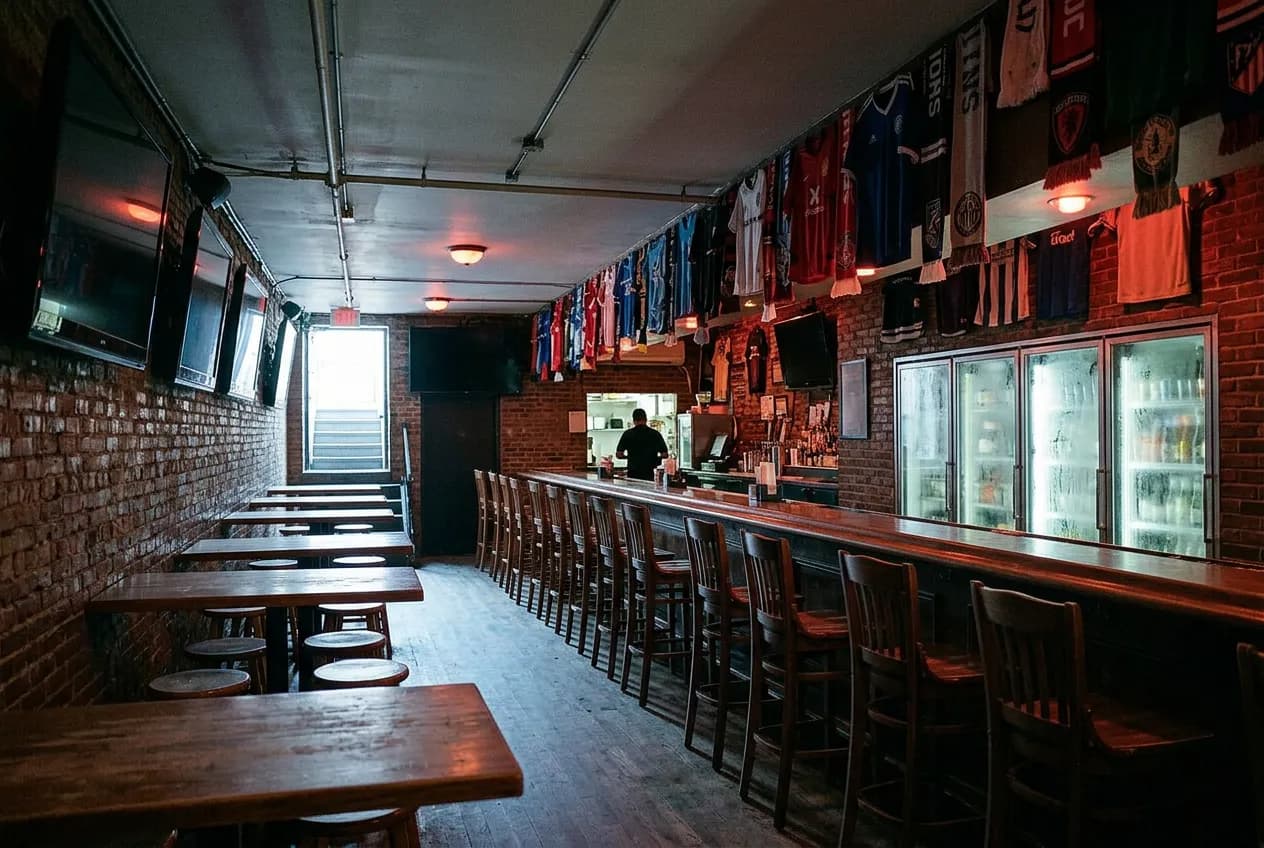 Dim basement bar interior with rows of televisions and framed football memorabilia on the walls.
