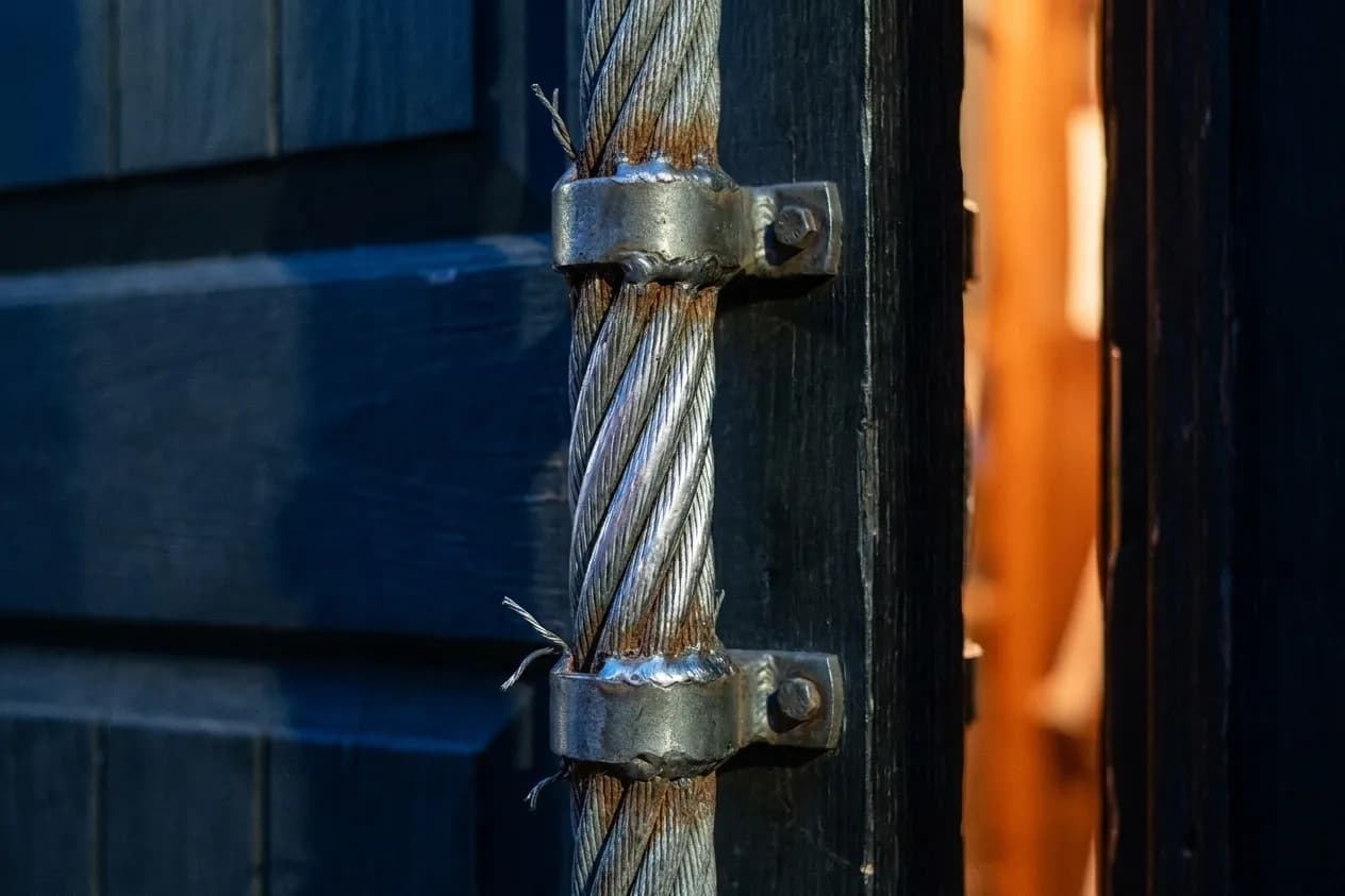 A close view of a heavy braided steel cable formed into a door pull on a dark timber door, worn bright where hands have gripped it