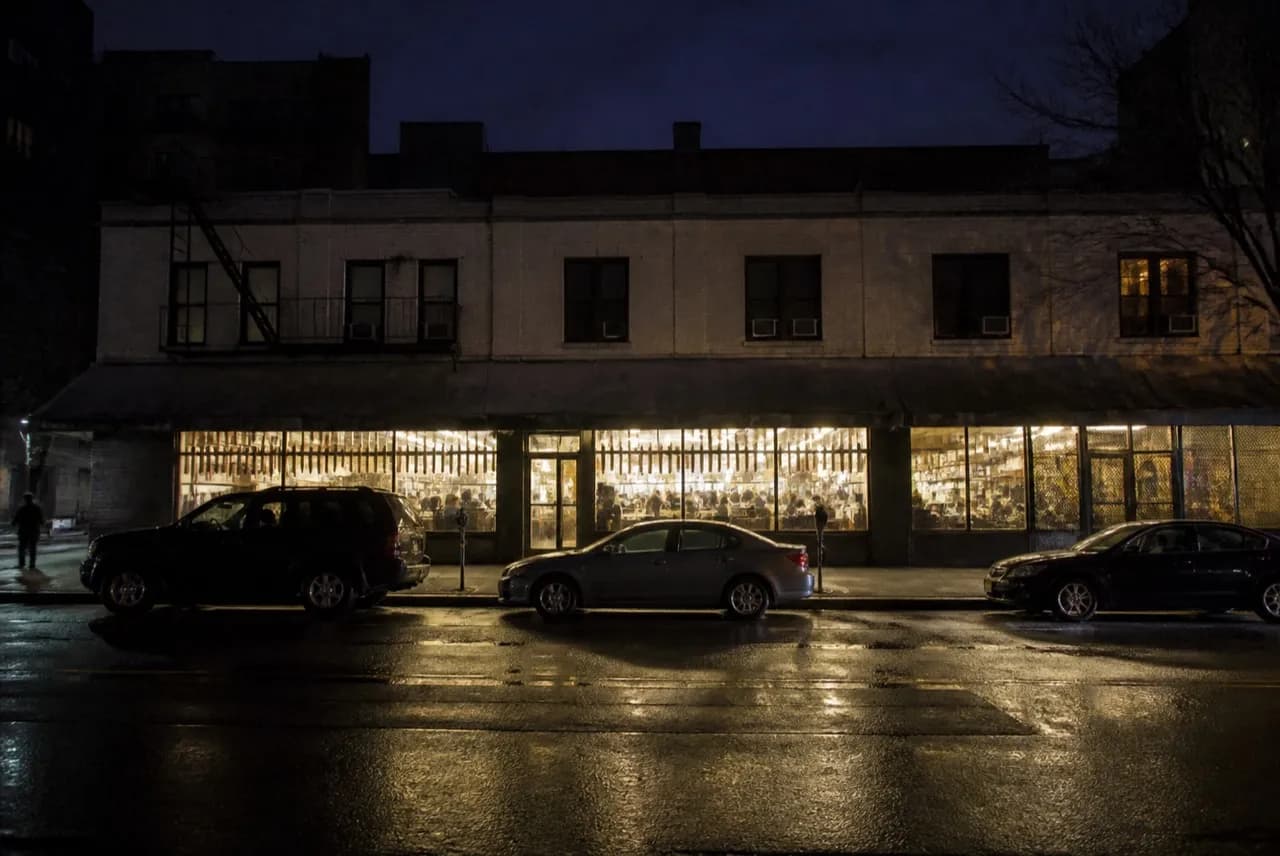 Late-night deli storefront on a wide Lower East Side avenue, lit windows and an empty sidewalk