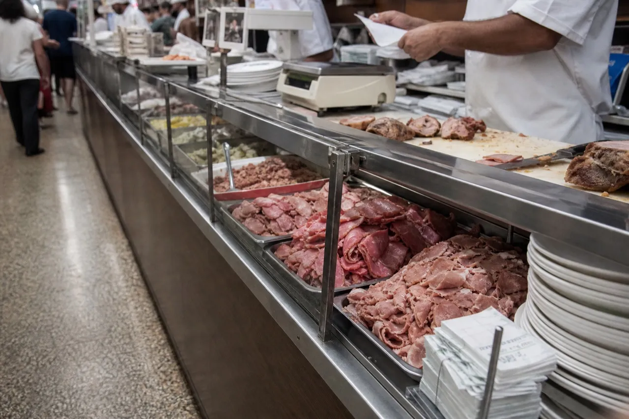 Deli carving counter at night with stacked trays and a line of paper tickets