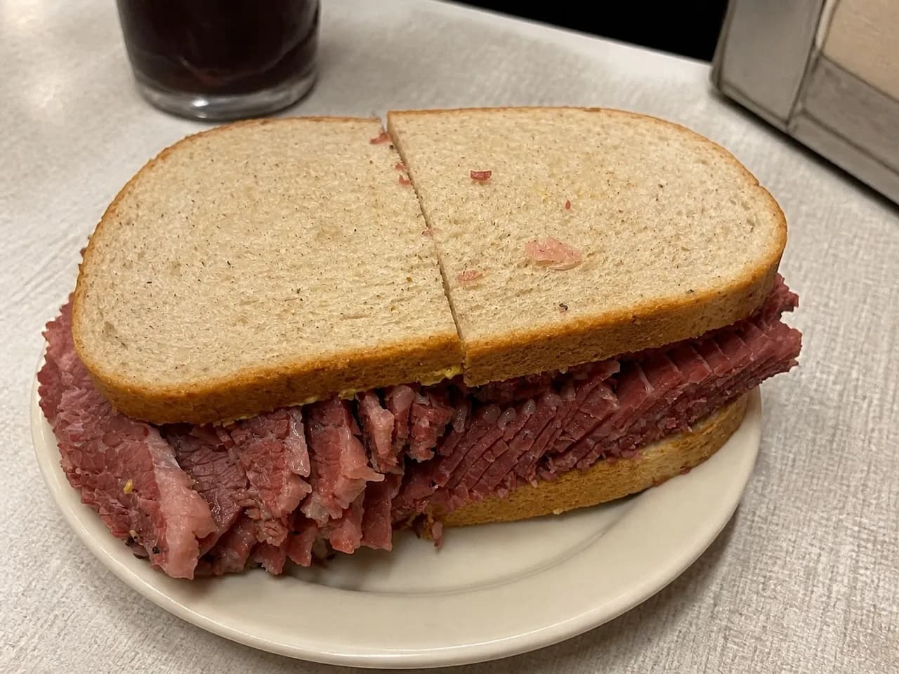 Hot beef sandwich on a paper plate on a scratched formica table under overhead light
