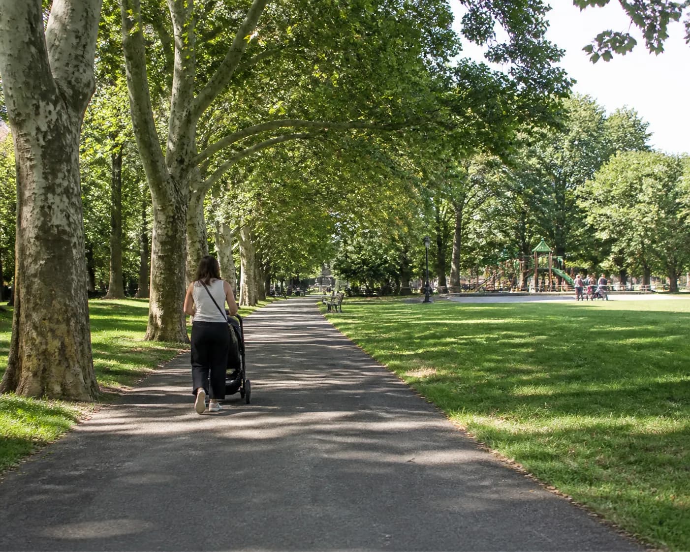 Tree-lined park path in Brooklyn with a stroller and open green space