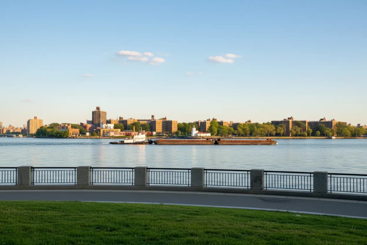 A wide East River view with a passing barge from a park
