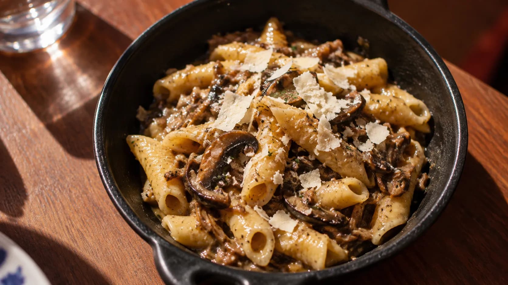 Overhead bowl of mushroom-ragu garganelli with pale ricotta salata on an L’Artusi dining table in bright directional light.