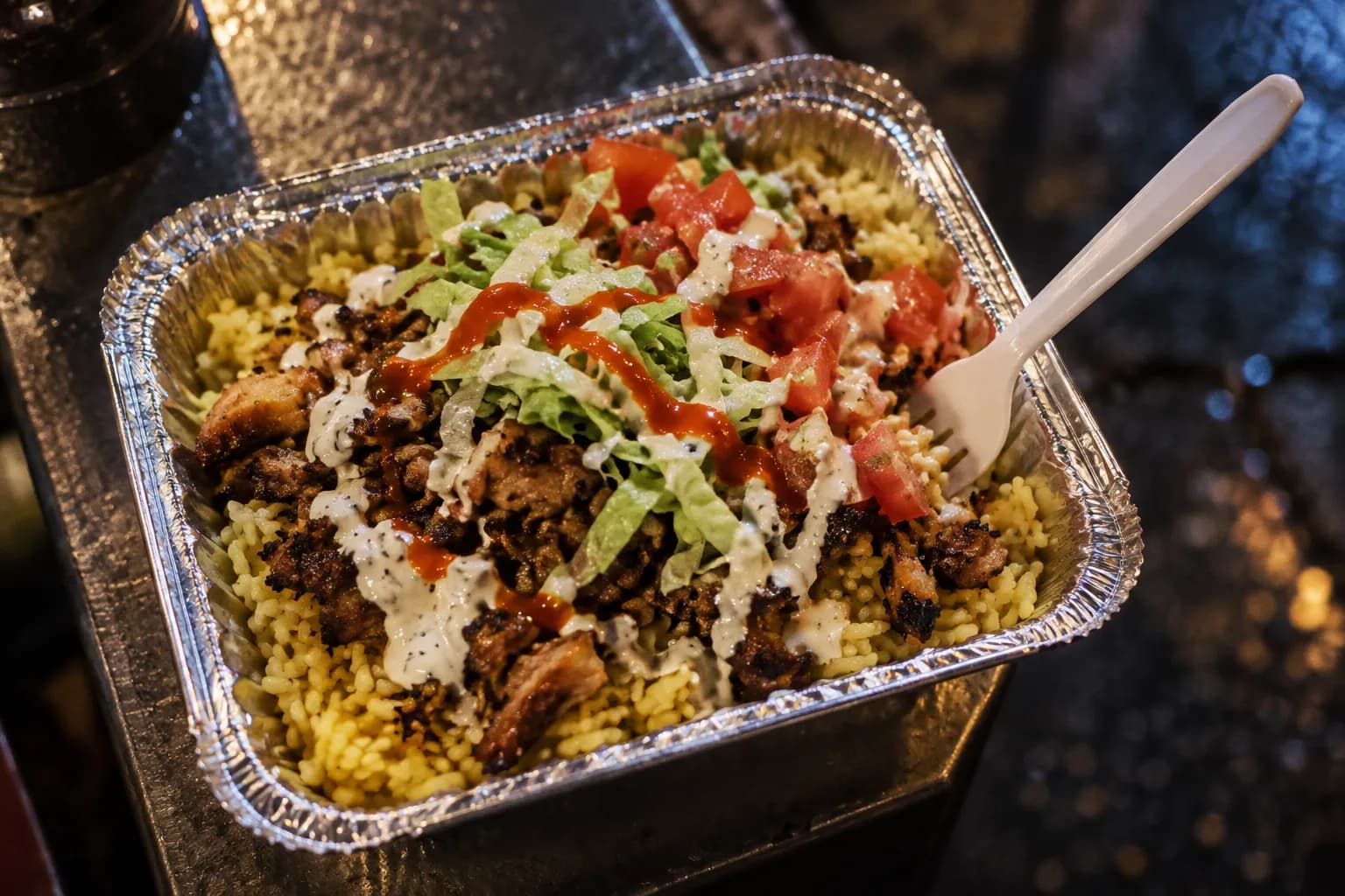 A foil platter of rice, chopped meat, lettuce and pale sauce