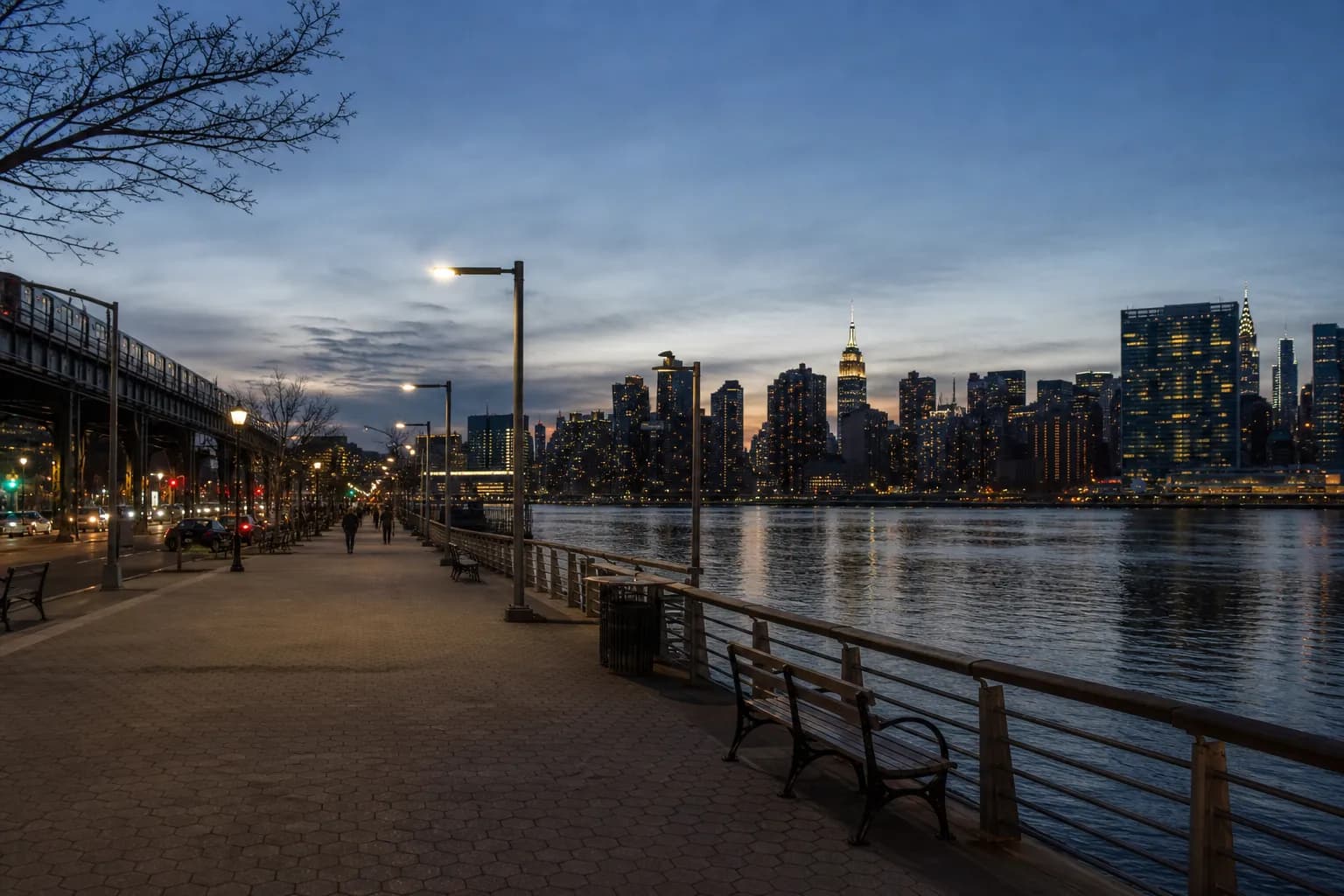 Queens waterfront walkway with skyline views at dusk near a subway-accessible park