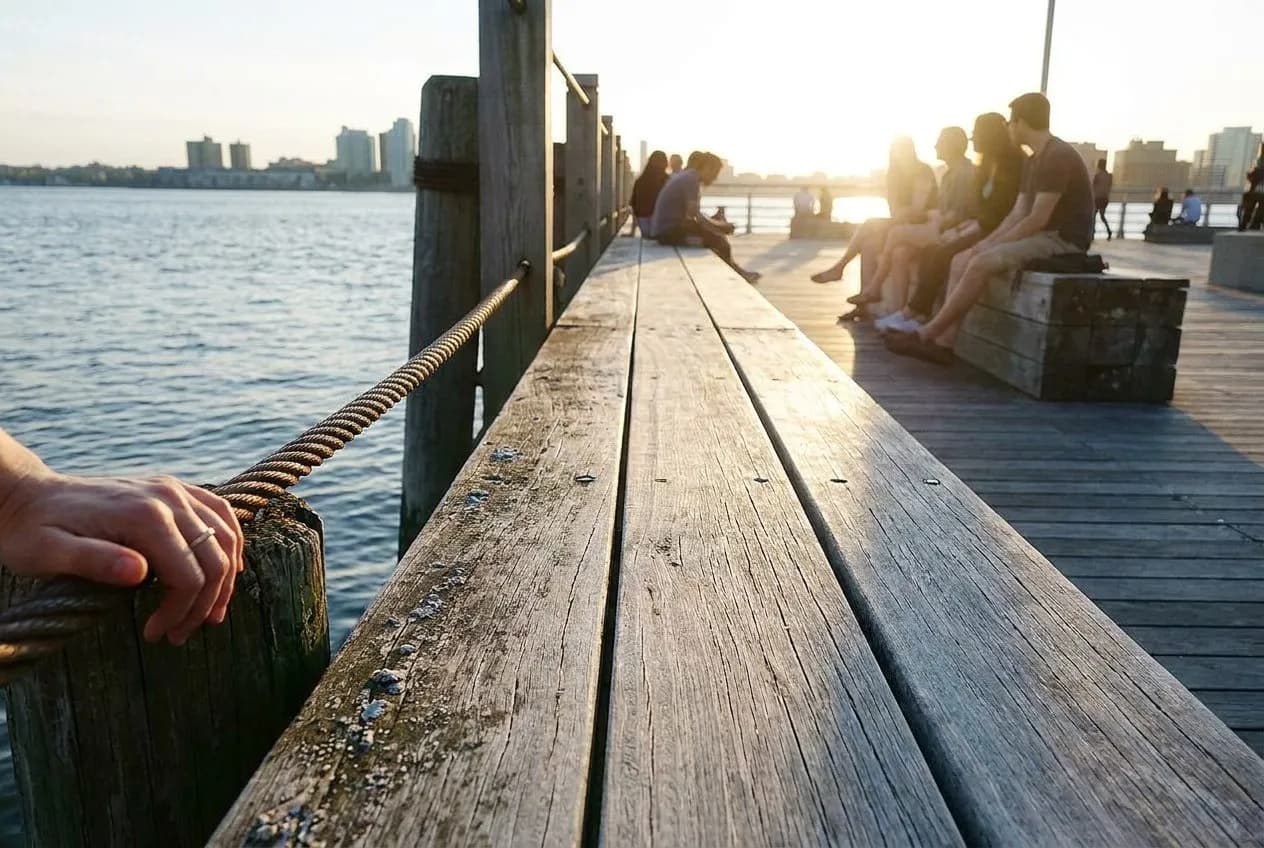 A weathered wooden Hudson River pier deck at golden hour with hazy shoreline across the water