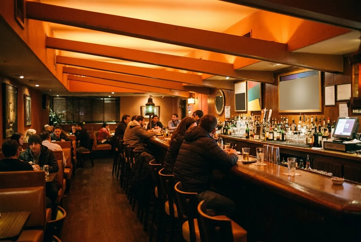 A long neighbourhood bar filling up in the early evening, stools taken end to end