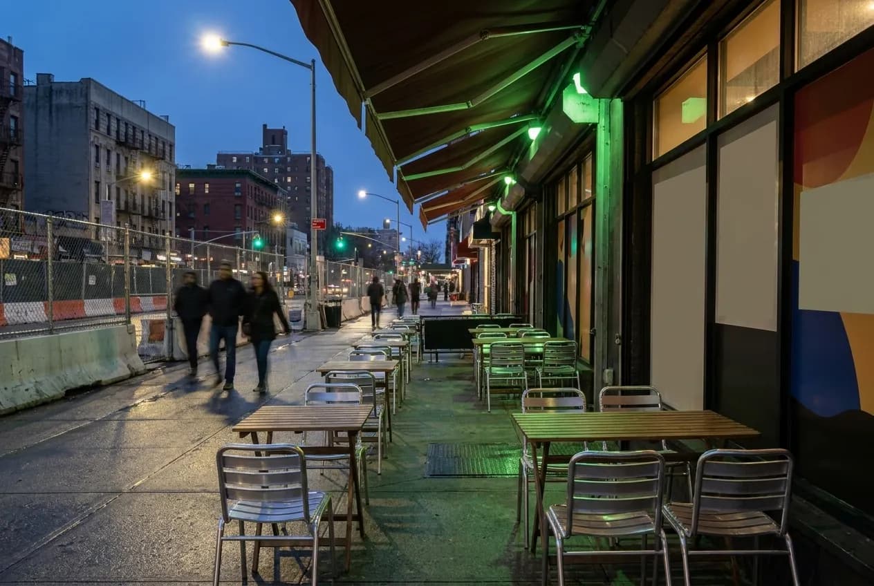 Sidewalk tables along a wide uptown boulevard at the start of the evening