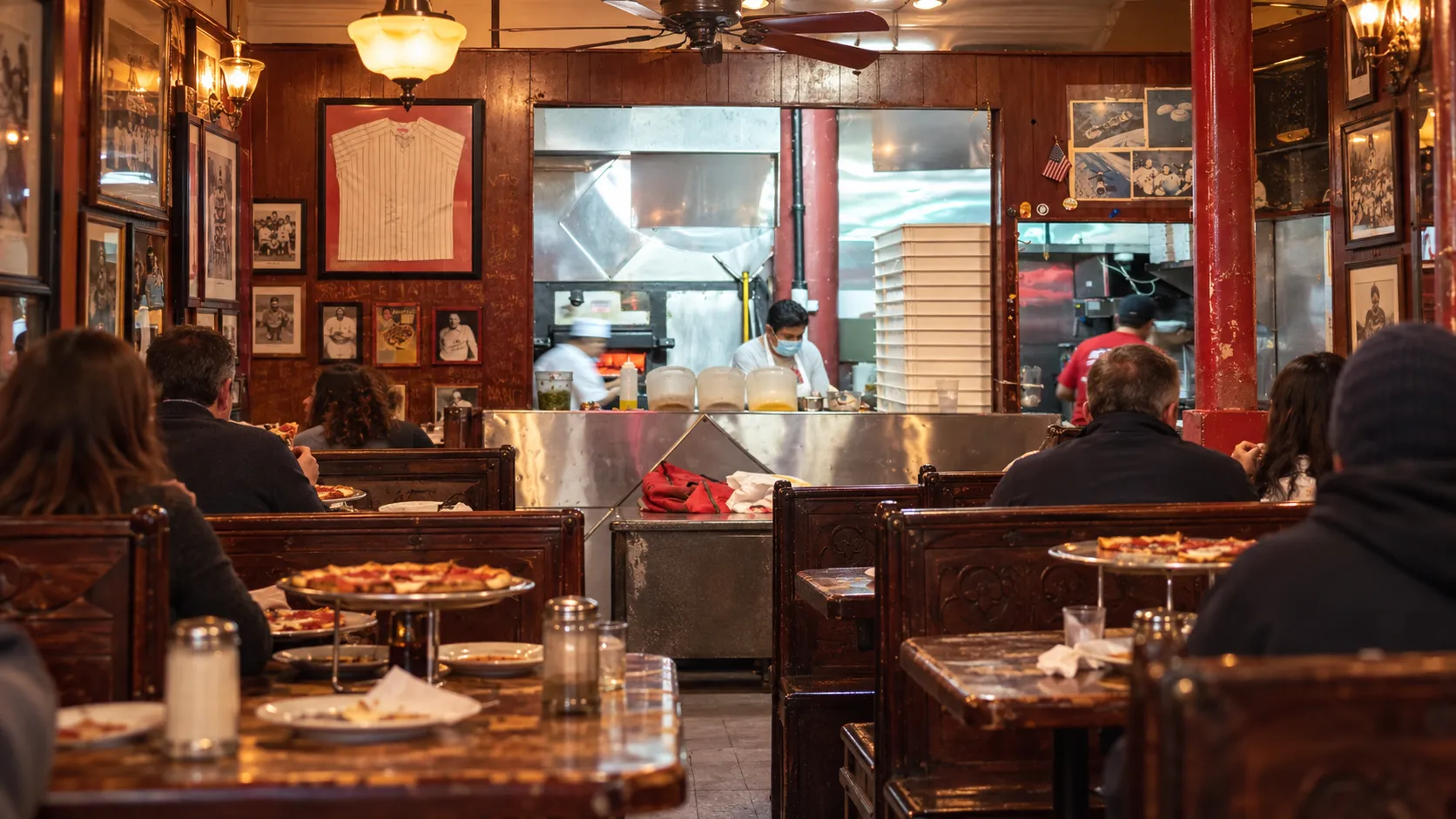 A wide interior view of John's of Bleecker Street's split dining rooms, dark carved booths, worn wood tables and warm amber light.