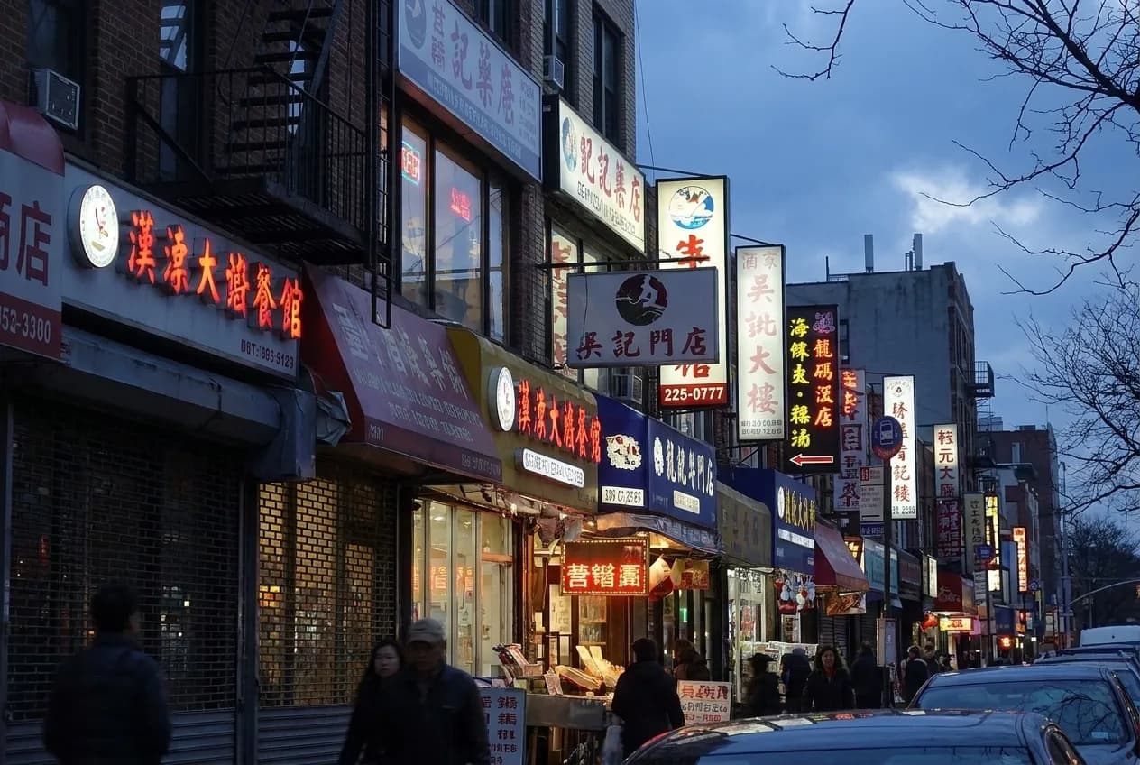 Dense shopfront signage along a commercial street in Flushing, Queens