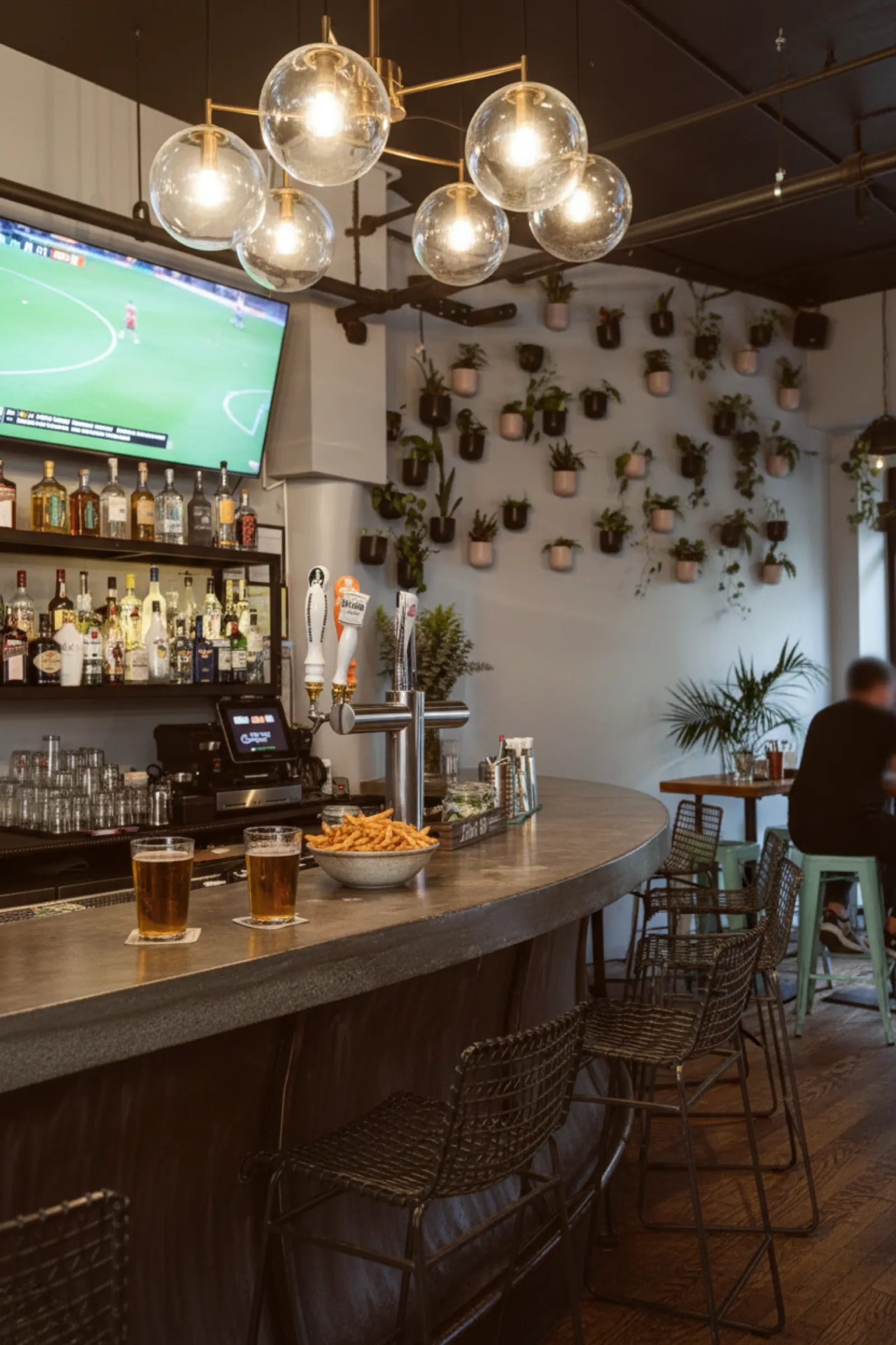 Concrete bar at Eastpoint in the East Village with beer taps, a plant-covered wall, and the game playing on the corner TV