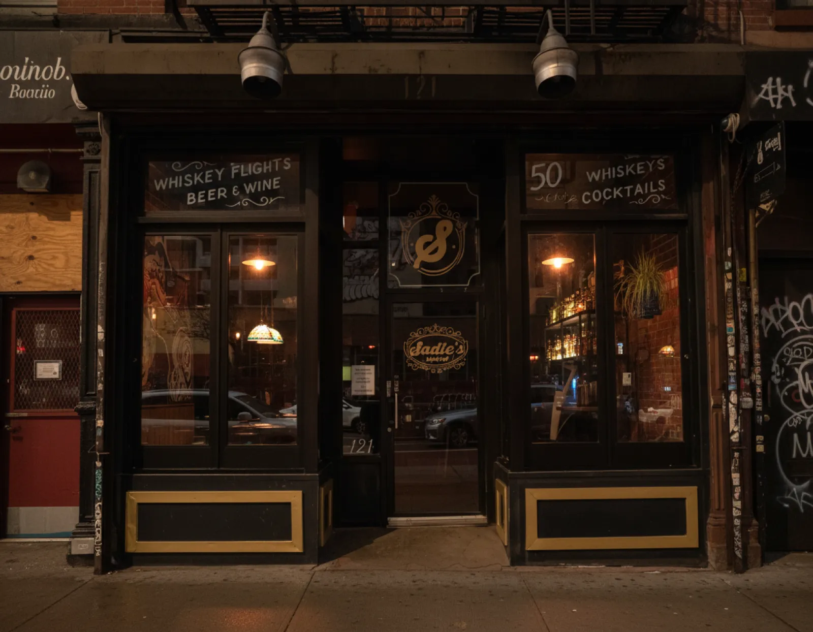 Night-time storefront of Sadie's Ward on Essex Street with gold-lettered windows and warm light spilling from the bar inside
