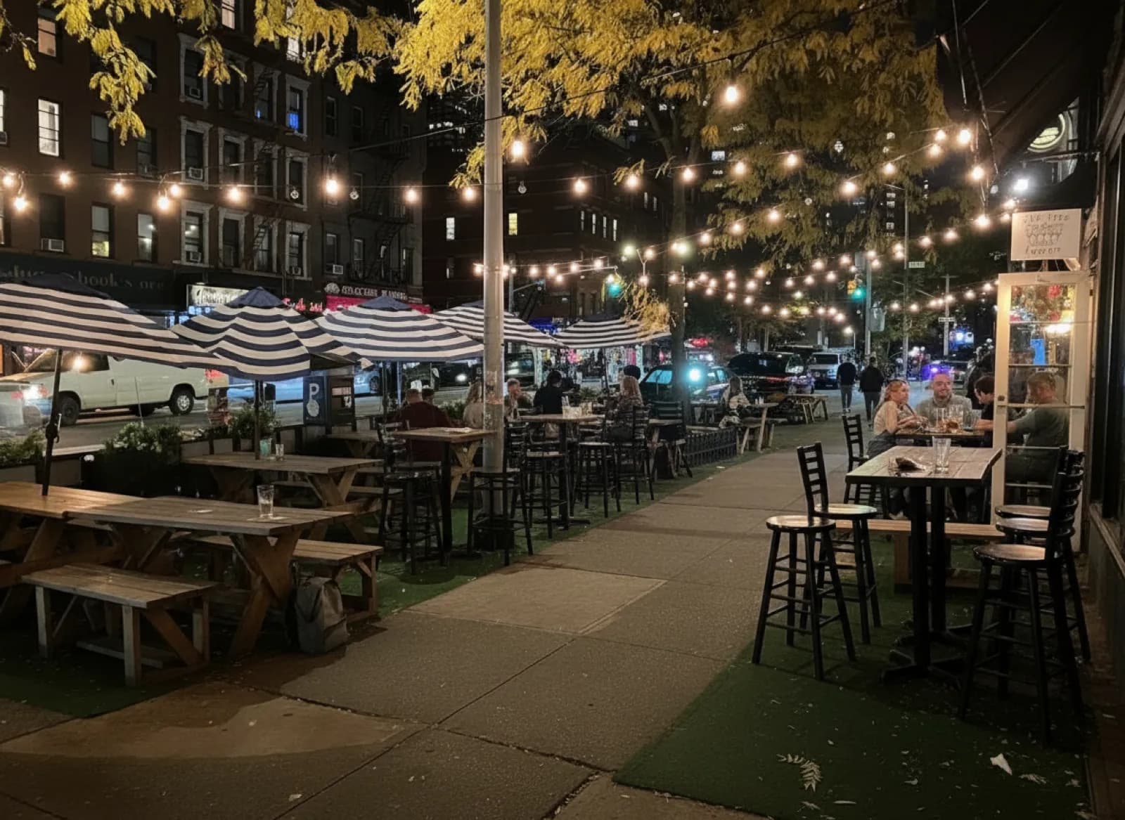 String lights over the sidewalk picnic tables and striped umbrellas outside The Five Lamps in Yorkville at night