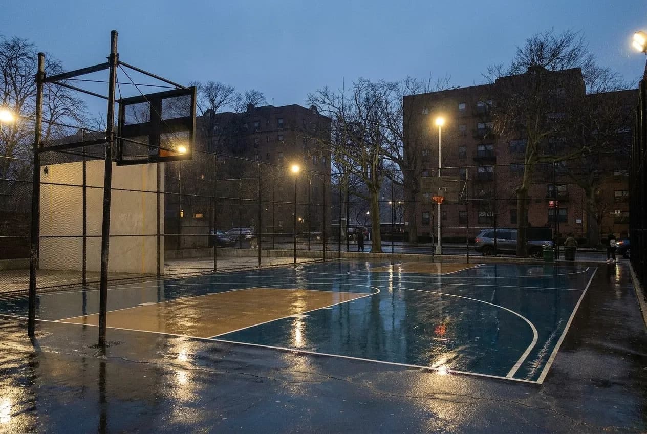 Floodlit outdoor basketball court in a New York park in the evening
