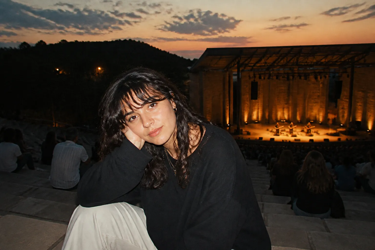 An outdoor amphitheater stage lit up at dusk with a seated audience