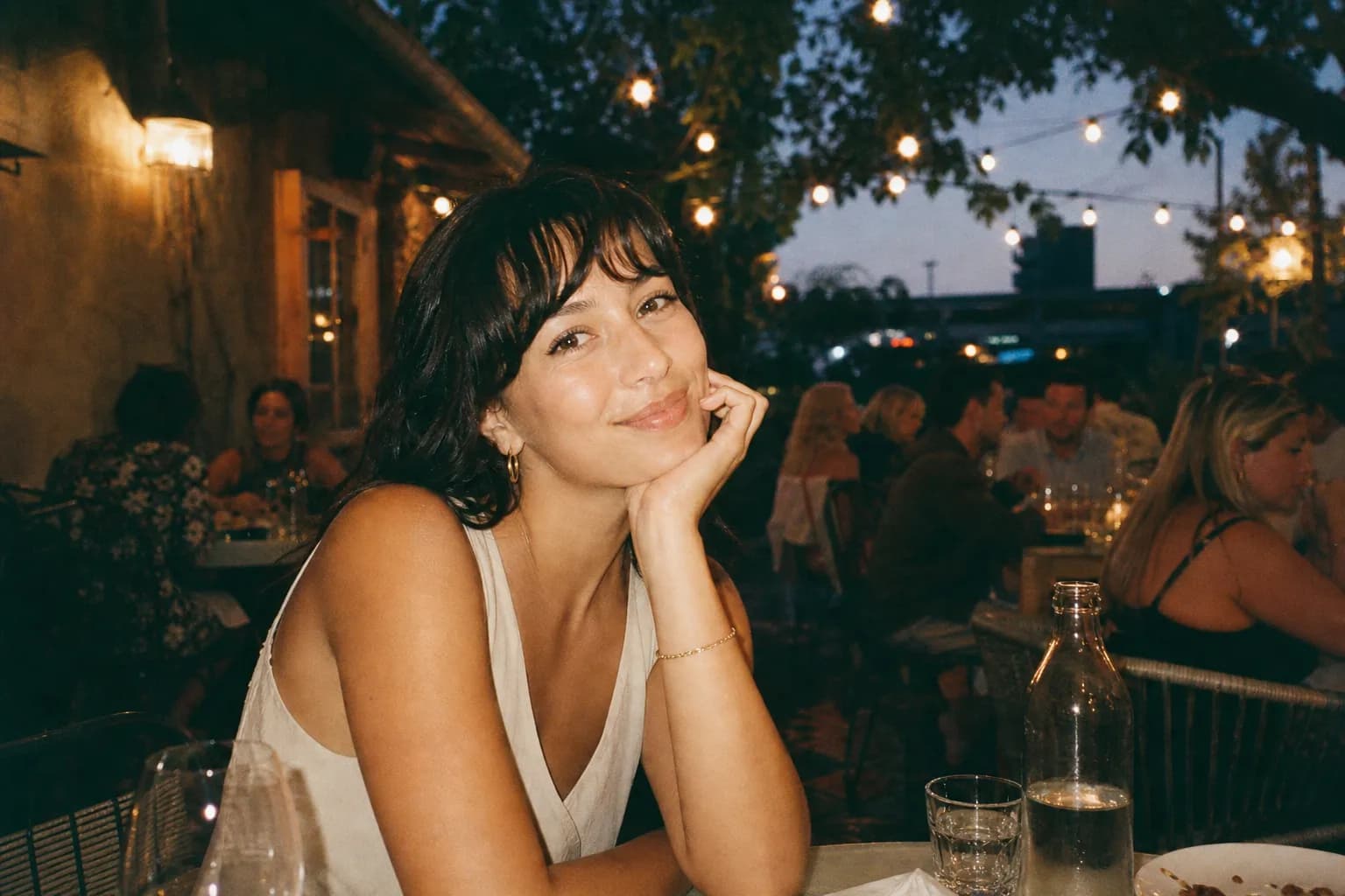 A string-lit restaurant patio with people dining outdoors at dusk