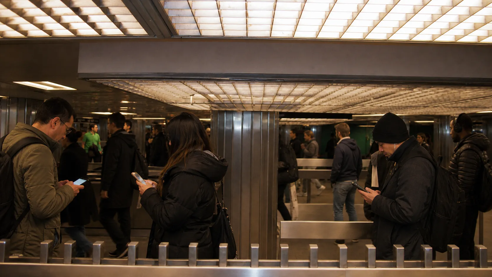 New York City subway commuters checking phones while waiting on a platform.