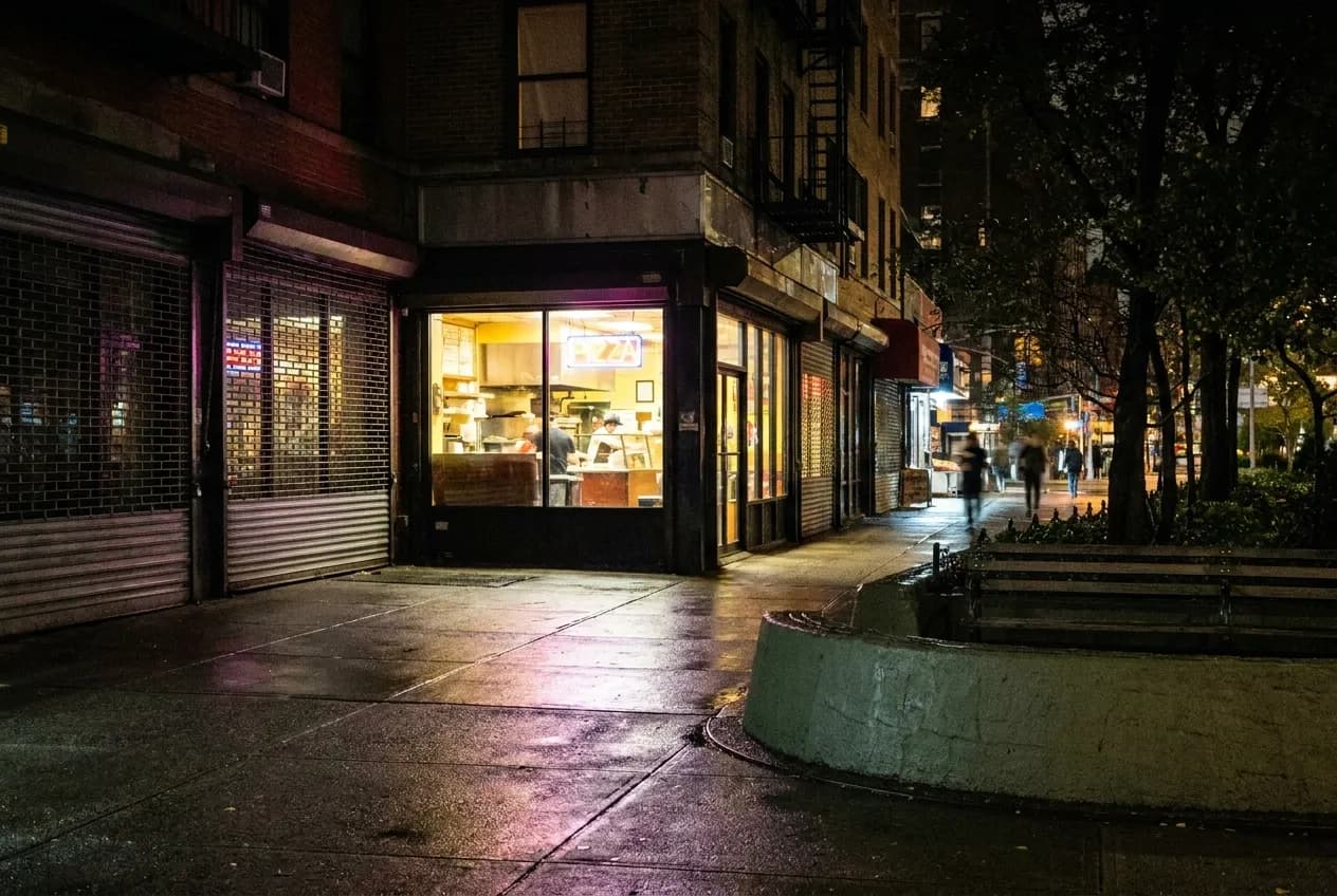 Late night pizza shop window glowing on an empty New York City street