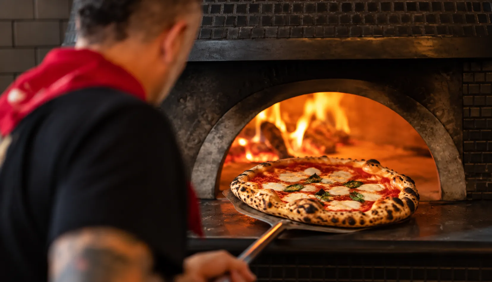 A Neapolitan margherita fresh from a wood oven with leopard-spotted crust, San Marzano tomato, fior di latte and basil on a metal peel
