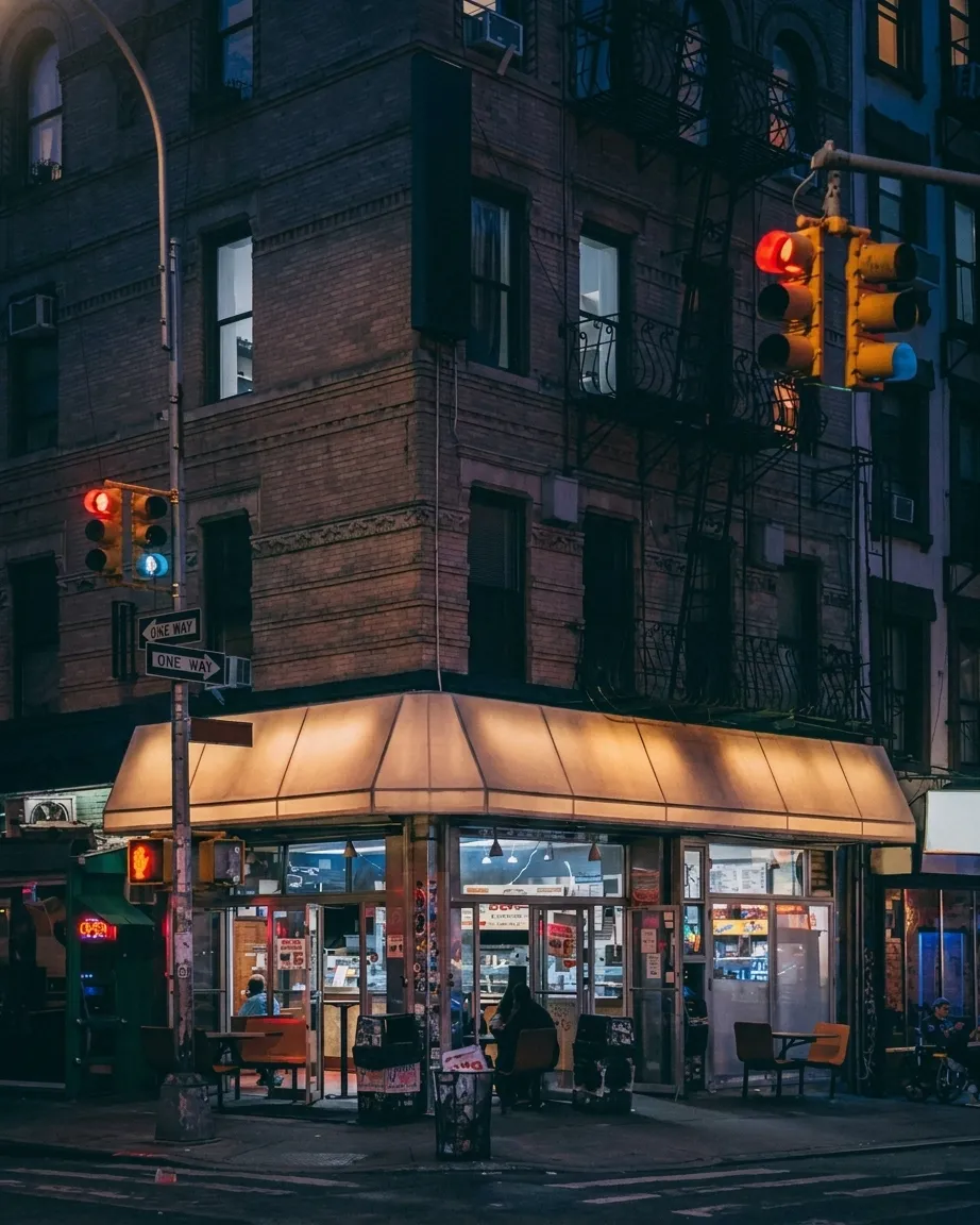 Slice shop exterior glowing at night on a New York corner with neon signage and a short line at the window