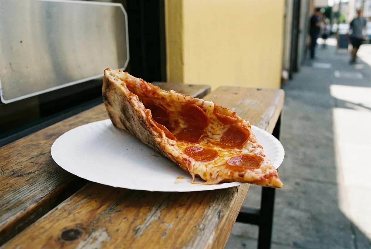 A large thin pizza slice being folded lengthwise over a paper plate