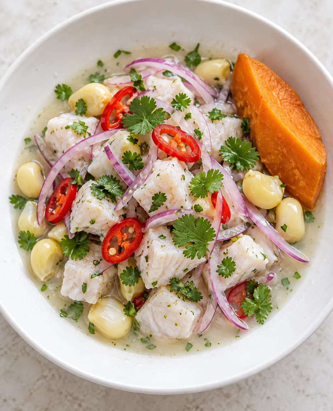 A shallow bowl of ceviche with red onion, chilli and corn in a pale citrus pool