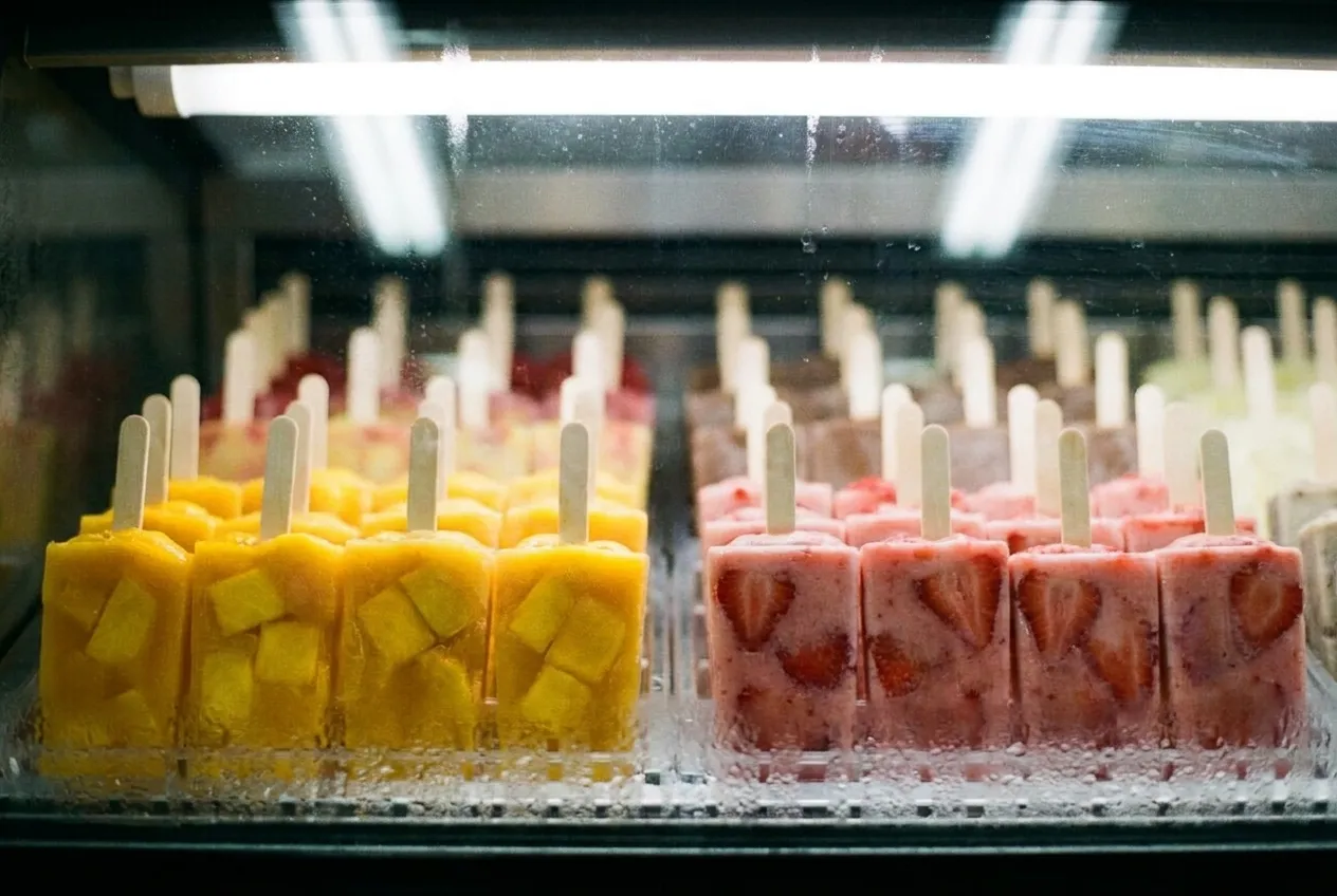 Colorful fruit paletas displayed in a freezer case with visible fruit chunks