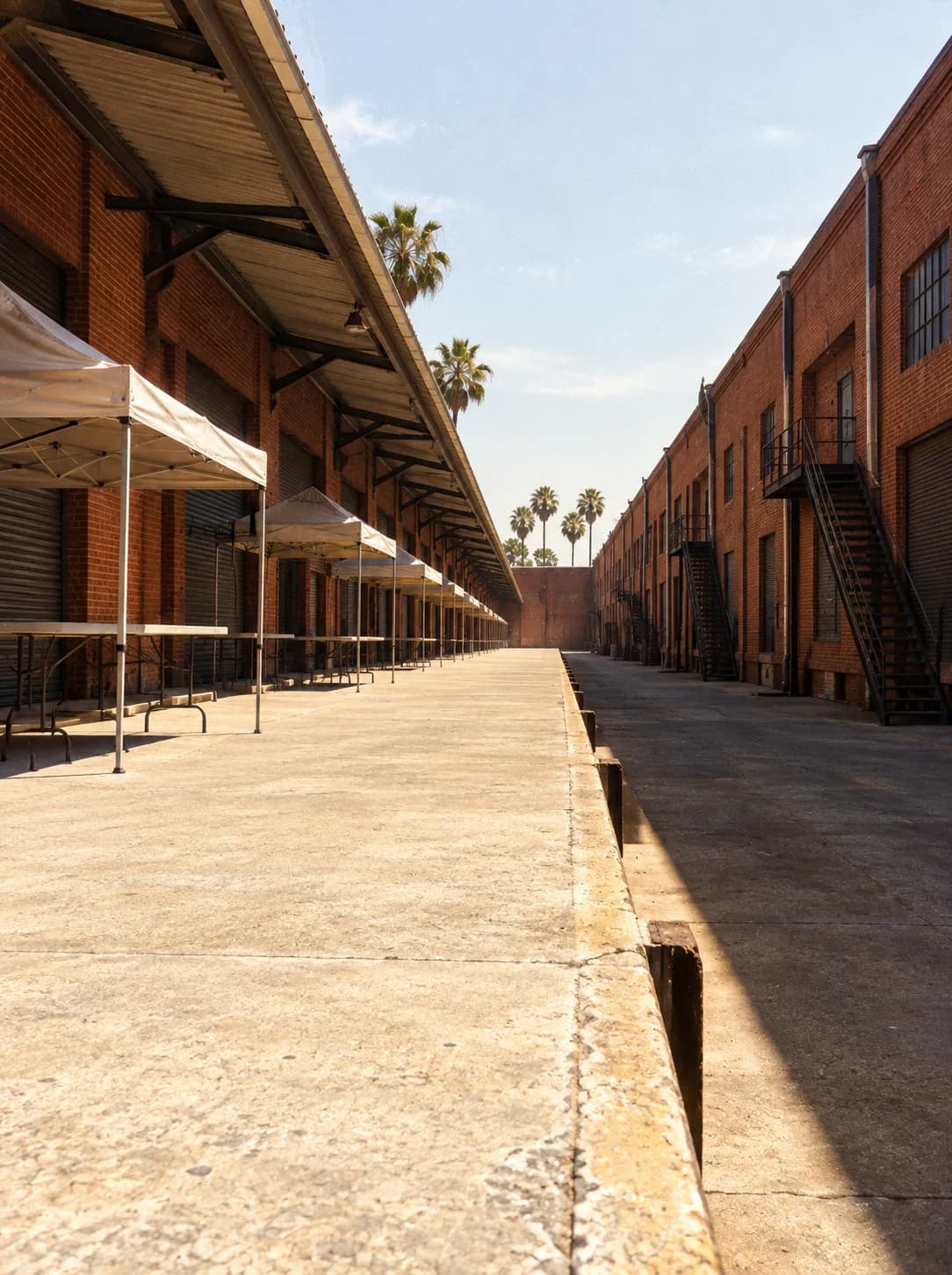 Market stalls set up along a wide loading dock between brick industrial buildings