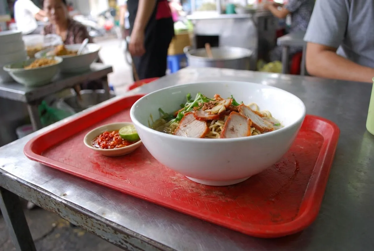 A bowl of noodles and a small dish of chilli on a plastic tray