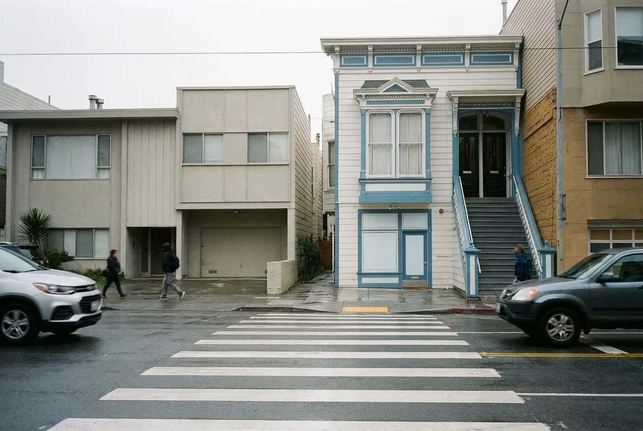 A San Francisco street with mid-century buildings and a wide crossing under grey sky