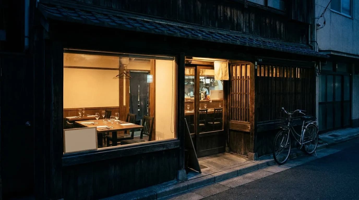 A small neighbourhood restaurant seen from the pavement at night, warm light through the window and a handwritten card propped in the corner of the glass