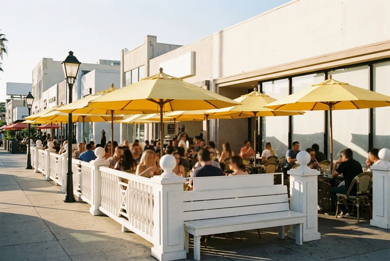 A sunlit sidewalk patio with yellow umbrellas outside a low storefront in Los Angeles