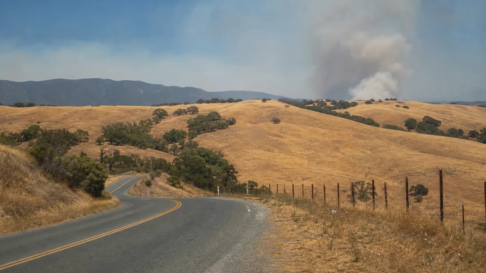 Dry hills and a rural road near Sunol with light smoke haze in the distance.
