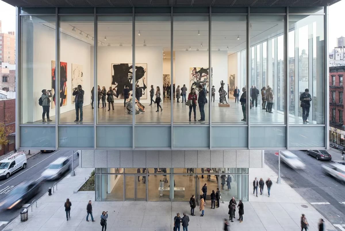 A contemporary art gallery interior with large bold artworks on white walls, visitors, and natural daylight through big windows