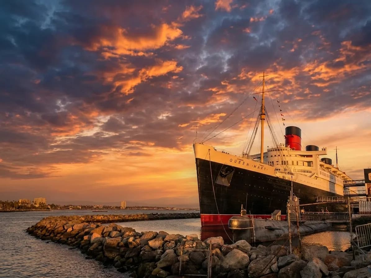 The Queen Mary ocean liner docked at Long Beach harbor with art deco funnels against evening sky