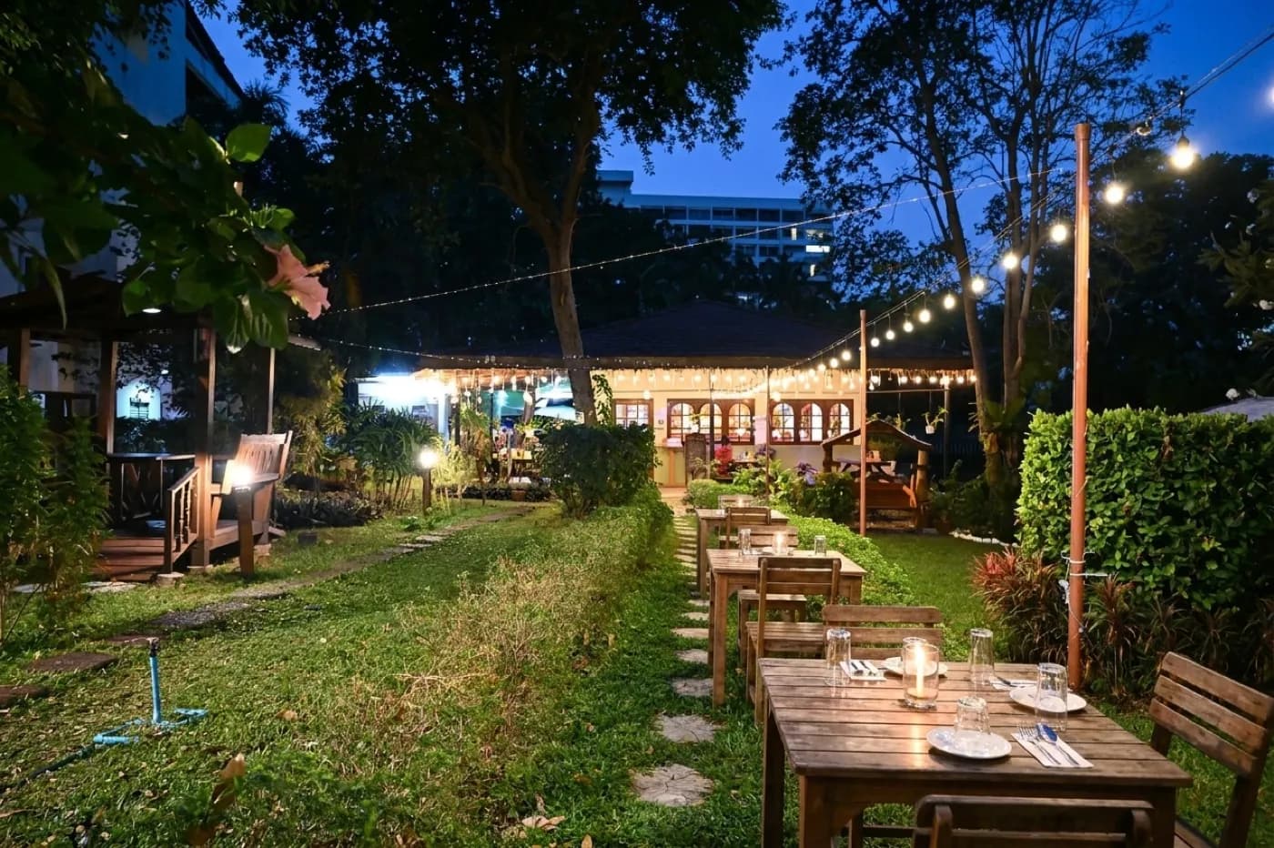 A quiet restaurant garden at dusk with a few wooden tables under string lights, ivy on a brick wall and no other diners