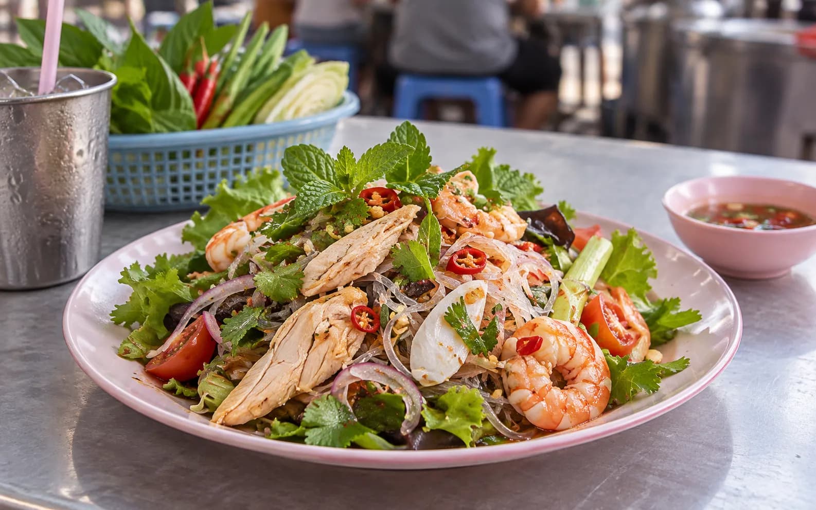 A plate of Thai street food with fresh herbs and chillies on a simple laminate table