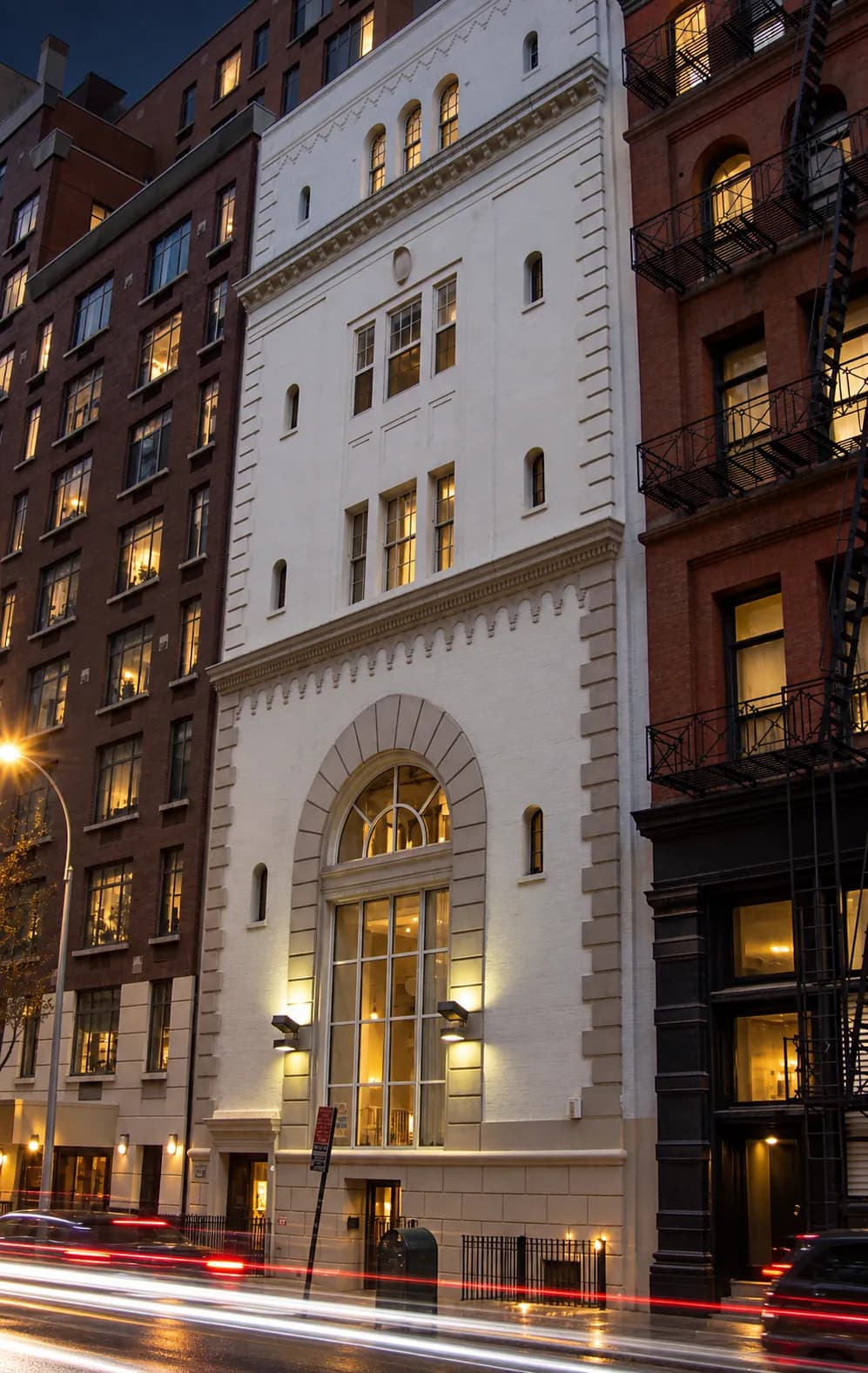 Midblock Manhattan street at night with cast-iron and limestone frontages and headlight trails passing