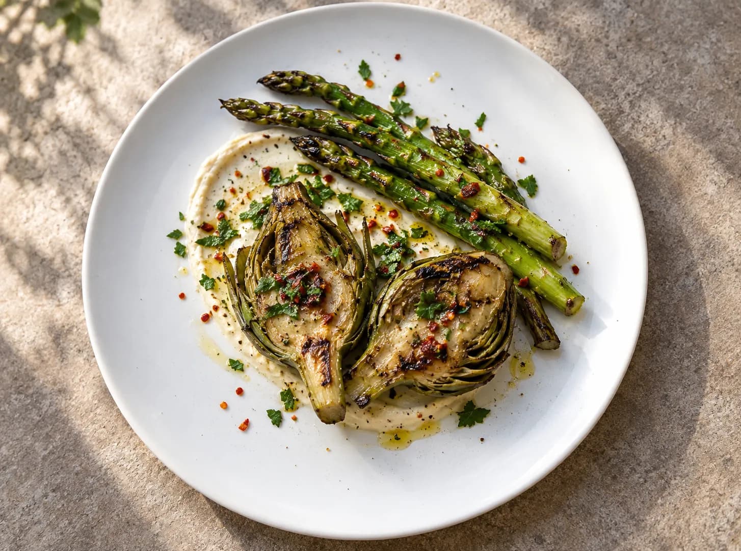 Shared plate of charred asparagus and halved artichokes with grill marks over a smear of pale sauce