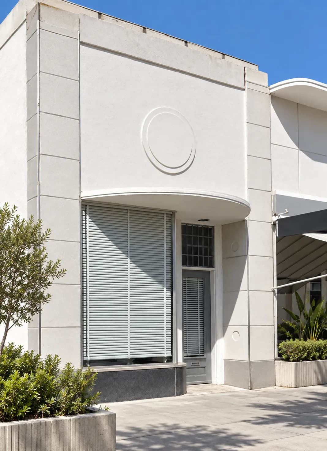 White rendered facades with deep reveals and a shaded colonnade above raised planting beds