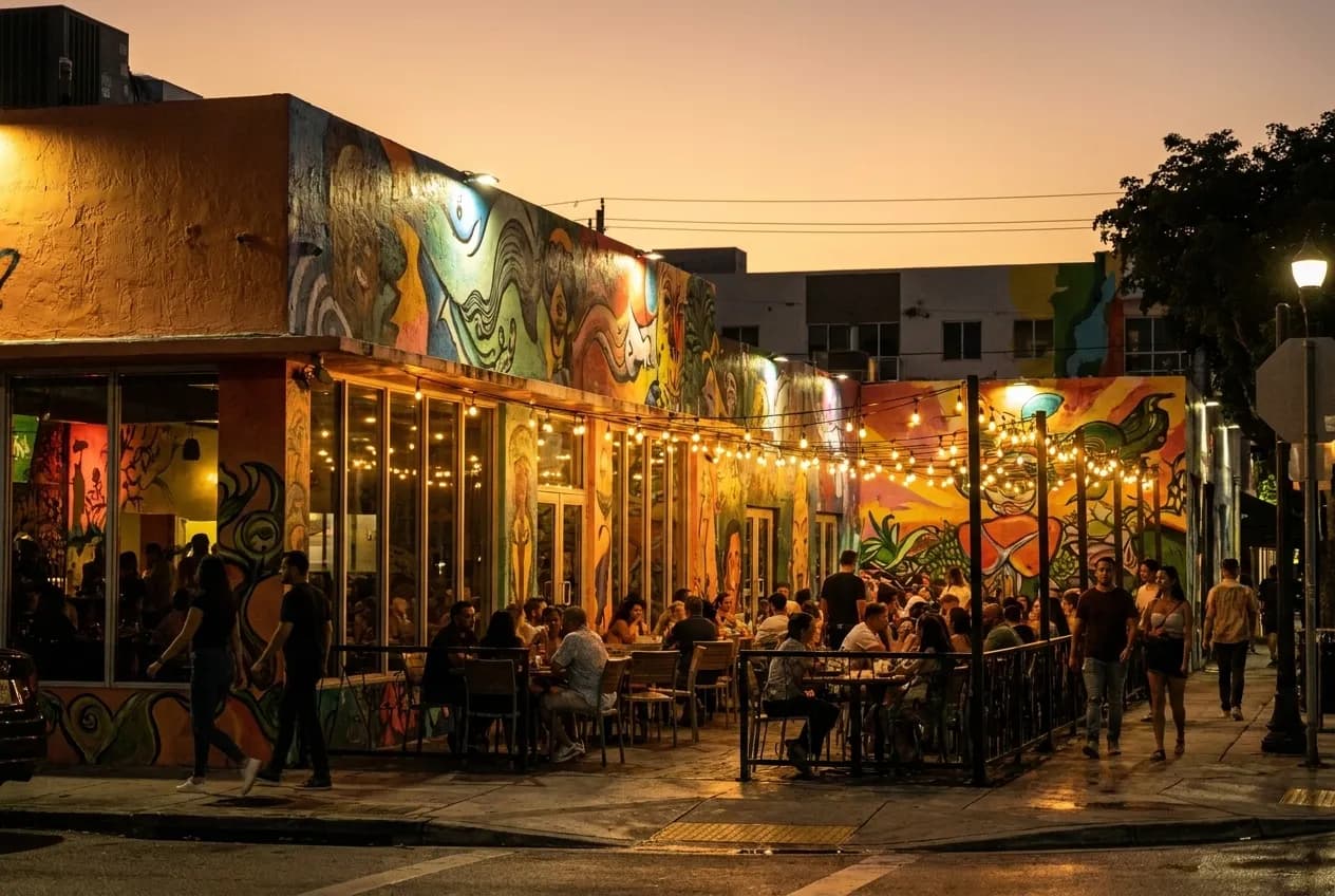 Wynwood street at dusk with painted building facades, low streetlights, and restaurant patios beginning to fill under warm artificial glow.