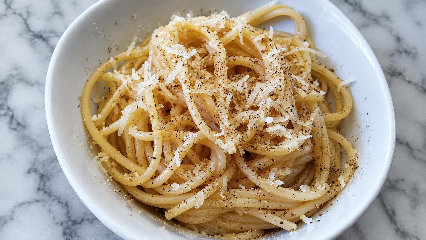 Shallow white bowl of long pasta twisted into a nest with a glossy cheese and pepper emulsion