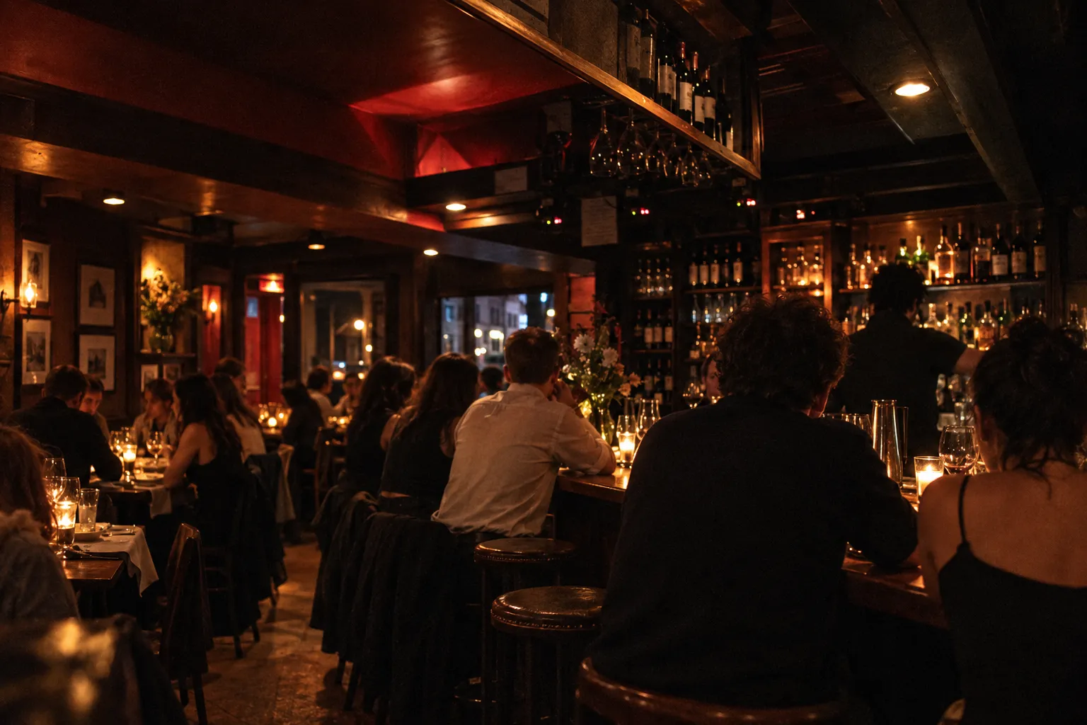 A small crowded upstairs dining room late at night, a long bar with occupied stools seen from behind and tables tight along the opposite wall