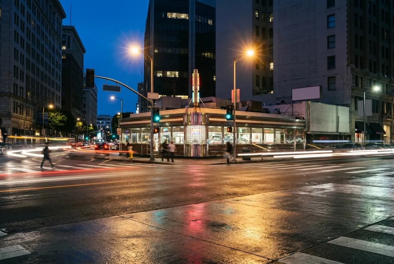 A classic diner building on a downtown Los Angeles street corner at night with streetlights and passing traffic
