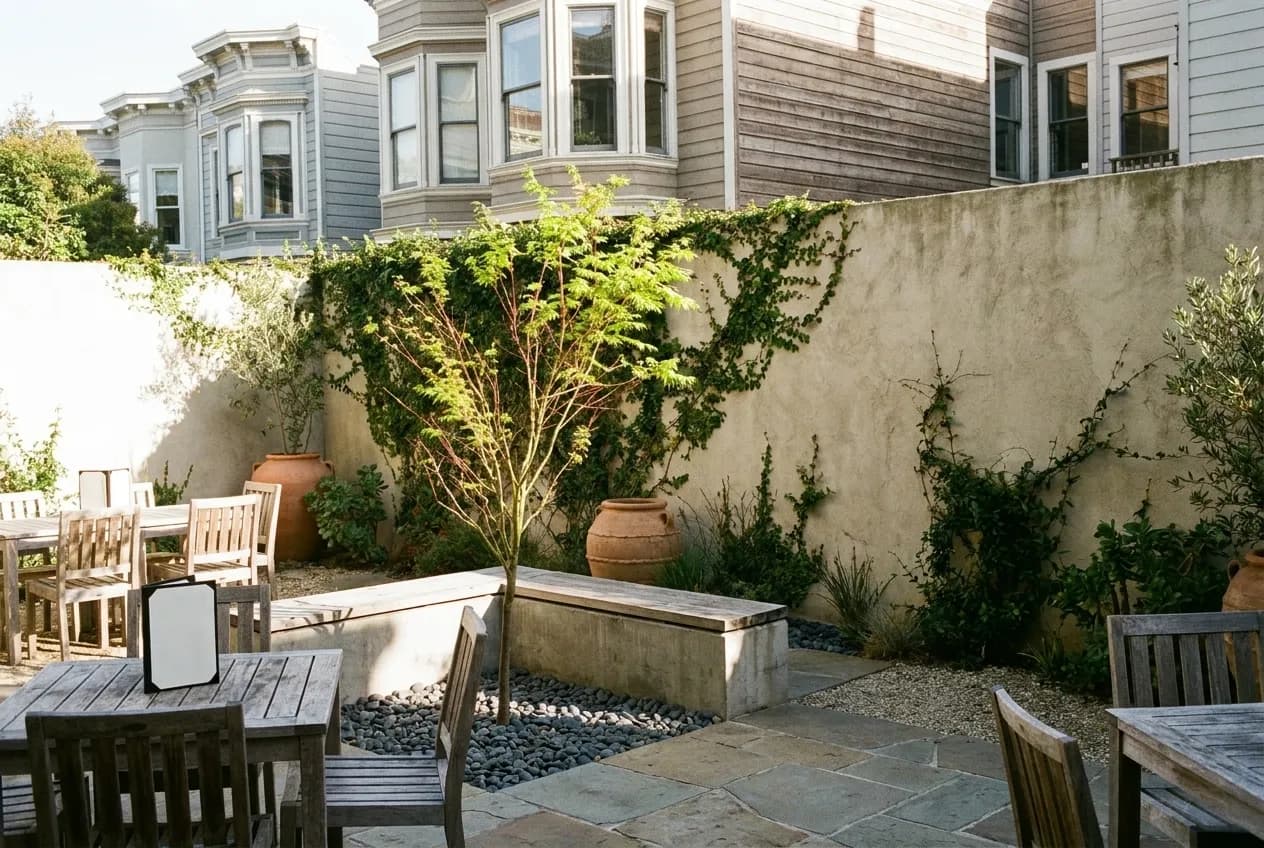 A sunlit restaurant courtyard in San Francisco with wooden tables and a high stucco wall